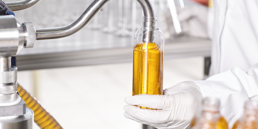 A person in a white lab coat holds a bottle and filling golden colour cosmetic product